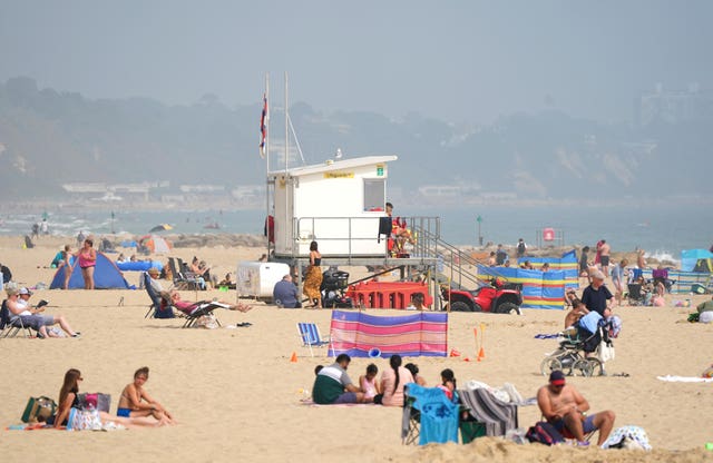 Sunbathers on a sandy beach, with a lifeguard tower in the centre of the photo