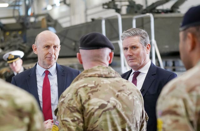 Two men speak to another man wearing camouflage and a dark beret