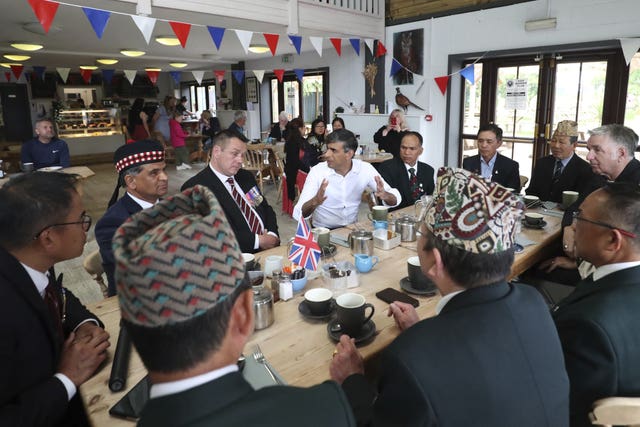 Rishi Sunak sitting at a long table under red, white and blue bunting surrounded by former servicemen 