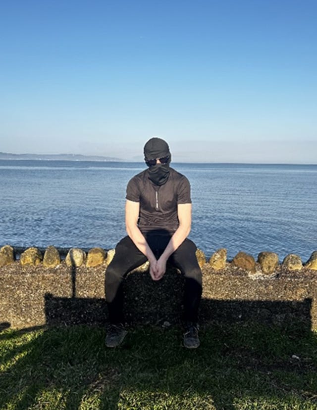 Alex Edwards sitting down while wearing a black head covering and sunglasses