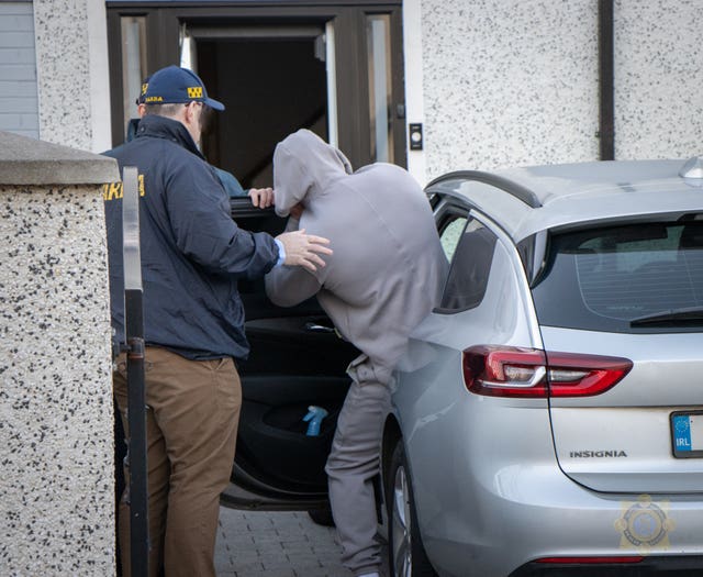 An arrested man is placed in the back of a car