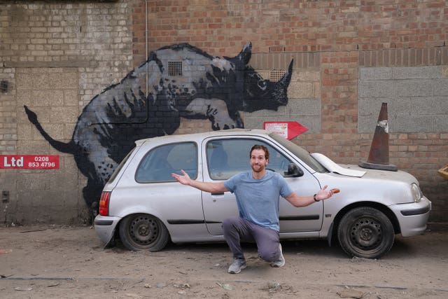 A man poses next to Banksy's rhino art work on a street in London