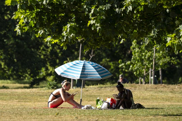 People read beneath a parasol during the hot weather in Hyde Park, London