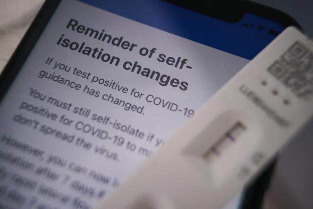 A positive lateral flow test cassette placed next to advice from the NHS Covid app on an iPhone, in London (Yui Mok/PA)