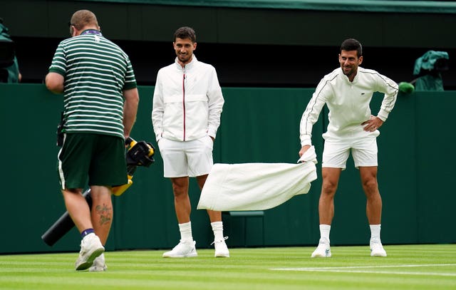 Novak Djokovic watches the ground staff try and dry the court 