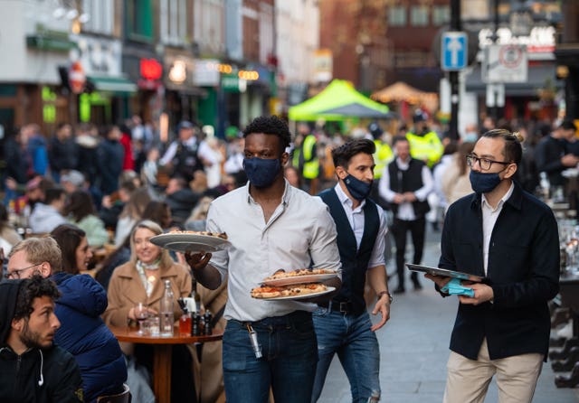 Male waiter carries plates of food to customers in busy outdoor restaurant