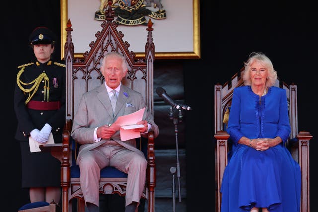 The King and Queen sit side by side in ornate chairs