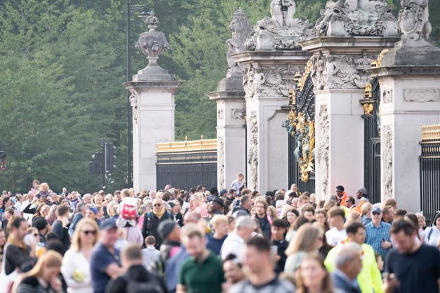 A side view of a crowd of people outside the gates of Buckingham Palace.