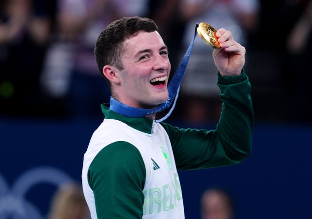 Ireland’s Rhys McClenaghan shows off his gold medal by raising it up, with a smile on his face