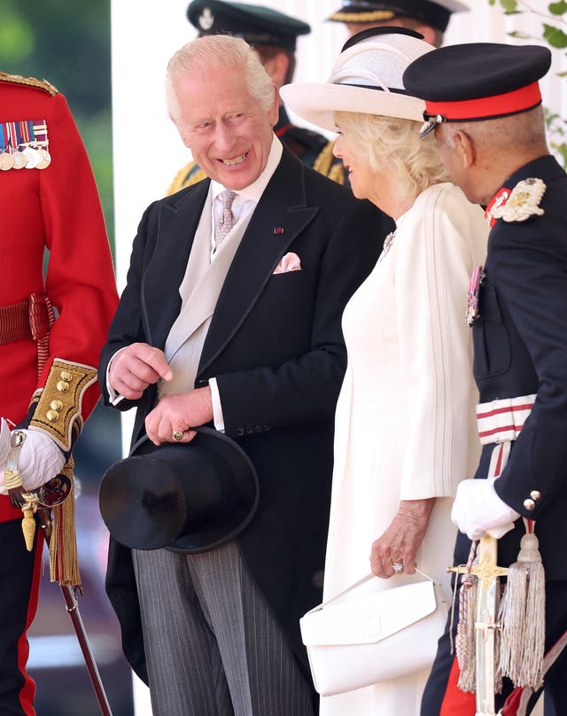 The King, holding his hat, smiles as he chats to Camilla