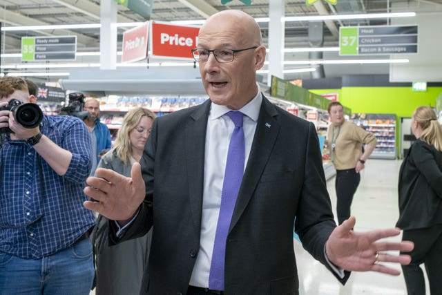 John Swinney will hands raised, talking to the media during a photocall in a supermarket