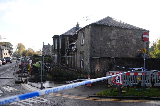 Photograph down the street of police tape in front of a building that has damage to its front where an explosion happened