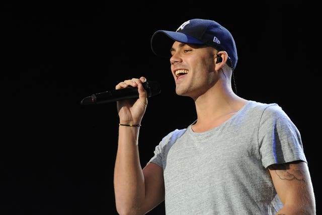 Max George in baseball cap, singing into a microphone