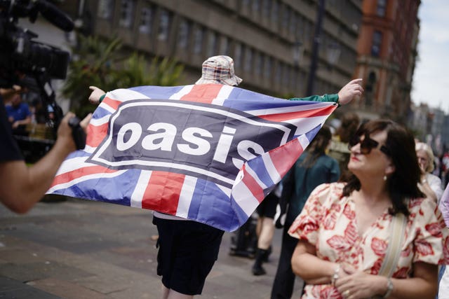 Oasis fan carrying a union flag featuring the bands name, and wearing a bucket hat