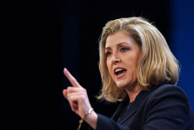 Penny Mordaunt, a blonde woman, is photographed mid-speech. She is gesturing with one hand