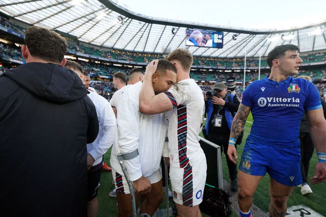 Ollie Lawrence, centre left, is embraced by Fin Smith while on crutches following England’s win over Italy