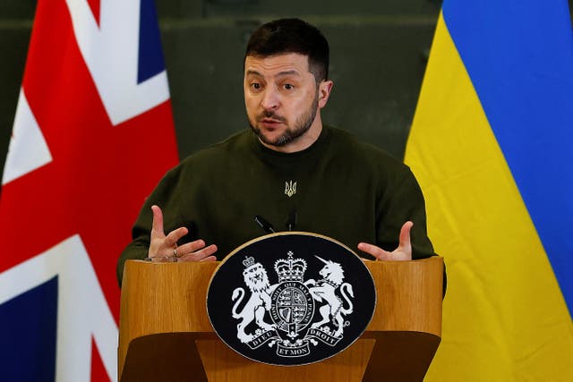 Volodymyr Zelensky speaking from behind a podium in front of UK and Ukrainian flags