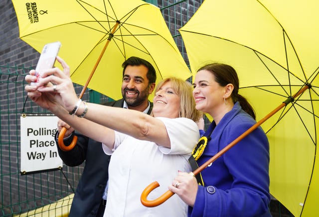 Three people take a selfie under yellow umbrellas
