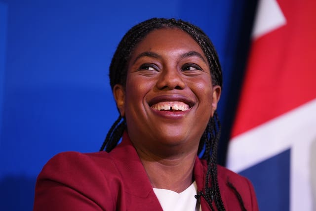 Kemi Badenoch smiles at a Conservative event, with a Union Jack behind her