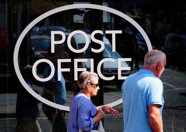 Two people walk by a large Post Office sign on a window