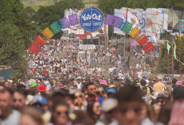 A sea of festival-goers walk beneath an arch and a sign - 