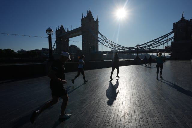 People jogging under a blue sky with the silhouette of Tower Bridge in London in the background 