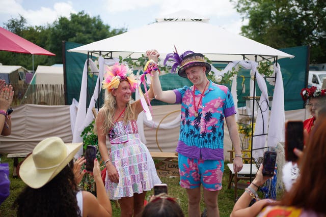 A couple wearing summery outfits hold up their arms, tied together at the wristsFestival 2024