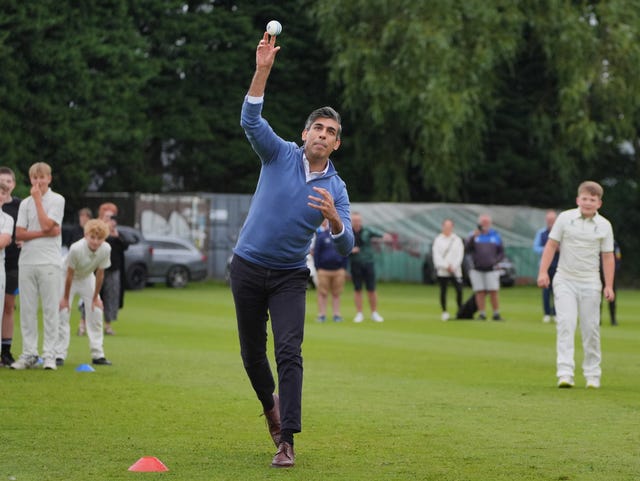 Rishi Sunak is watched by members of Nuneaton Cricket Club as he bowls a white cricket ball