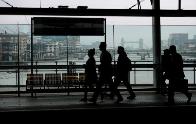 People walking at a station, with Tower Bridge and the Thames in the background