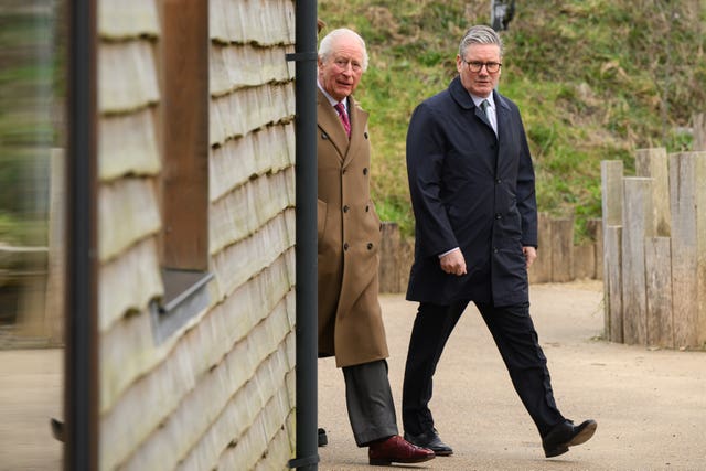 The King and Prime Minister Keir Starmer walk round the corner of a wooden building