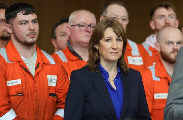 Rachel Reeves  standing in front of a group of workers wearing orange boiler suits