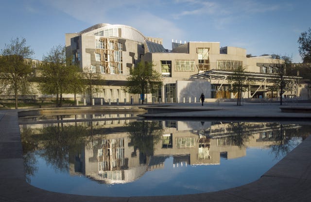 Exterior view of the Scottish Parliament building, with it also reflected in a pool in the lower half of the photo