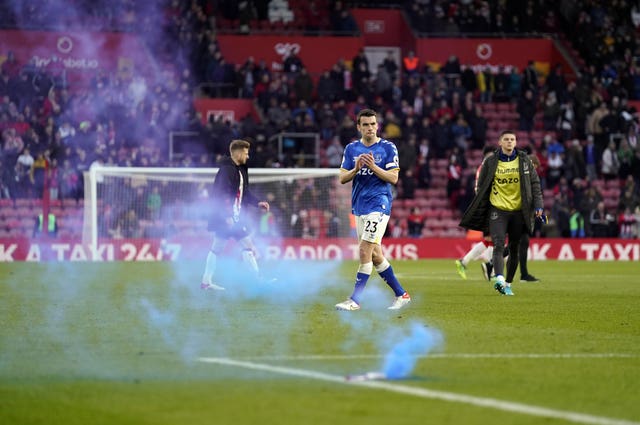 A blue flare lands on the pitch as Seamus Coleman applauds the Everton fans