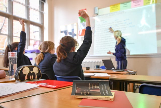 Children raising their hands during a lesson with a teacher in a school classroom