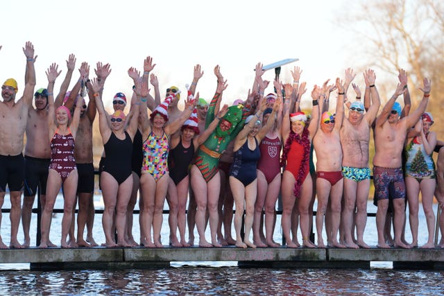 Swimmers, including some in fancy dress, standing at the edge of the Serpentine in Hyde Park with their hands raised in the air