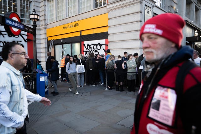 A queue of people wait to enter a shop with a sign above it reading Arts Arkade