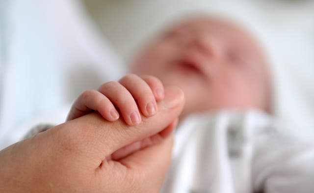 A newborn baby grasping a woman's thumb