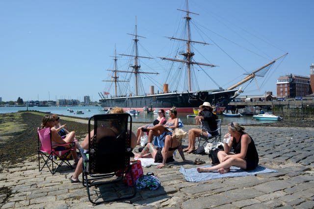 A group of people sunbathe in Portsmouth, near the HMS Warrior