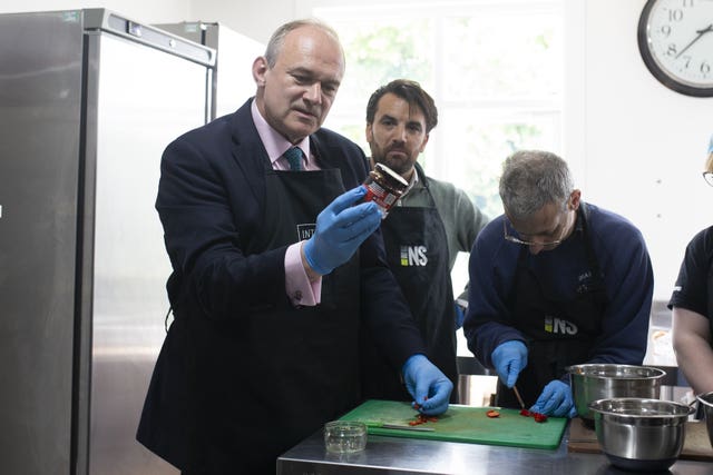 Sir Ed Davey examines a jar while alongside two workers in a kitchen