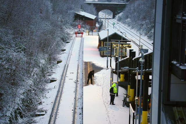 A worker clears snow from the platform at Hunt’s Cross station in Liverpool 