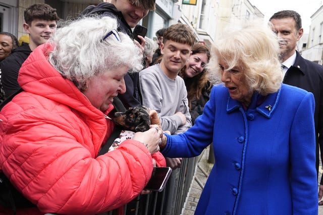 Camilla strokes a dog in the arms of a woman