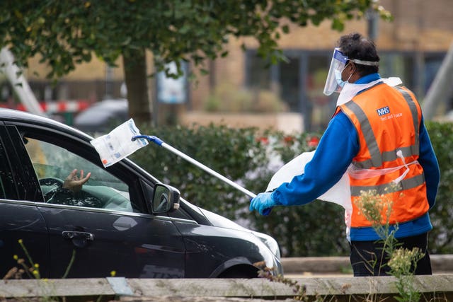 A member of staff collects a completed test kit from a visitor at a Covid-19 testing centre in Southwark, south London (Dominic Lipinski)