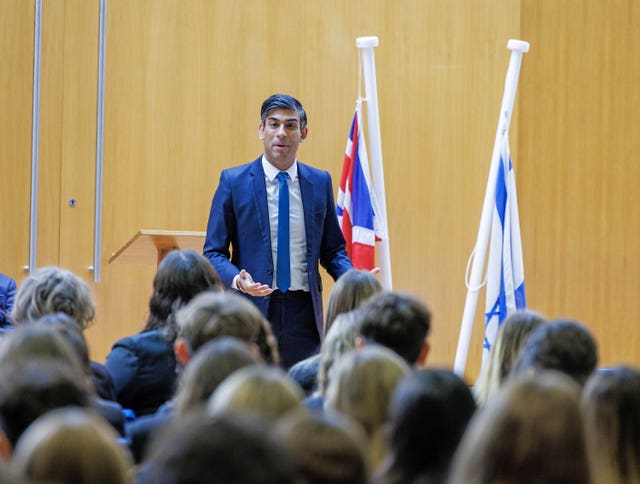 Rishi Sunak standing in front of the Union Flag and the Israeli flag speaking to students at the school .