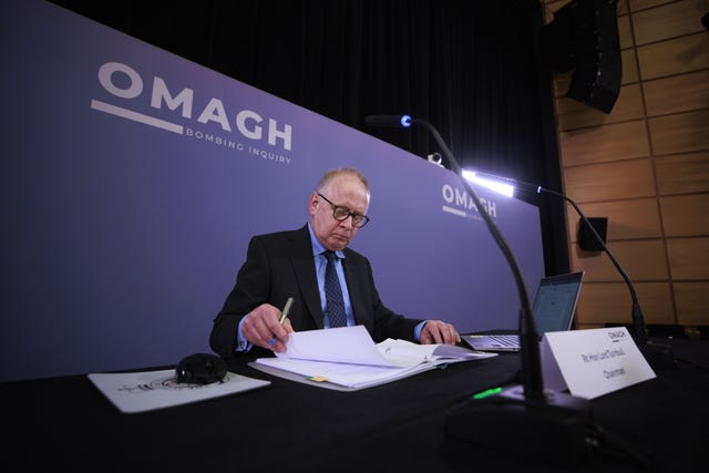 Chairman of the Omagh Bombing Inquiry Lord Turnbull reads notes at a desk in front of a purple background at the Strule Arts Centre in Omagh