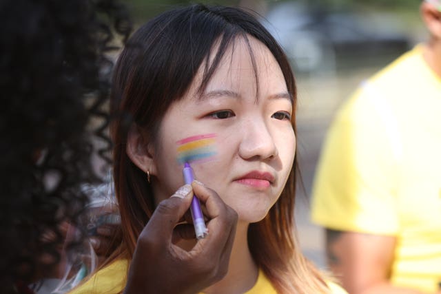 Pride volunteers add rainbow face paint to each other’s faces 