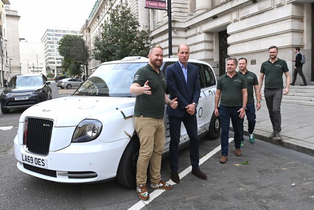 William stands in front of a white electric vehicle with ENSO staff 