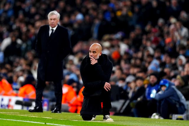 Manchester City manager Pep Guardiola kneels on the touchline with Real Madrid boss Carlo Ancelotti in the background