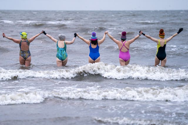 Women holding hands entering the sea in a line, seen from behind