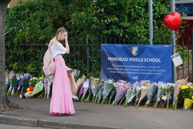 A woman looks at floral tributes at the entrance to Minehead Middle School in Minehead, Somerset