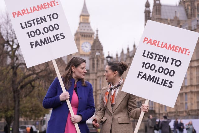 Theo Clarke, left, and Louise Thompson on College Green looking at each other while holding placards that read 'Parliament@ Listen to 100,000 families'